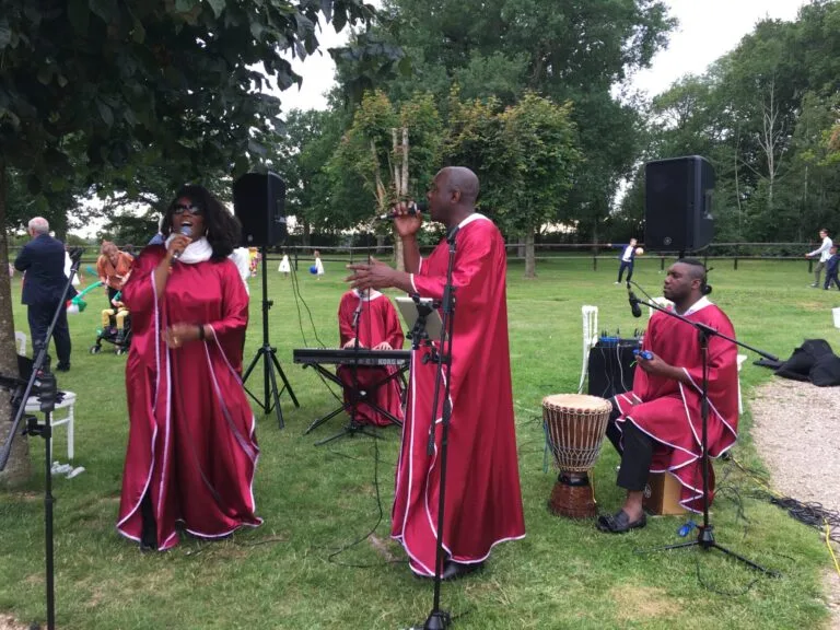 Amany, groupe de chanteurs en robes rouges se produisant en extérieur, accompagné d’un pianiste et d’un percussionniste jouant du djembé.
