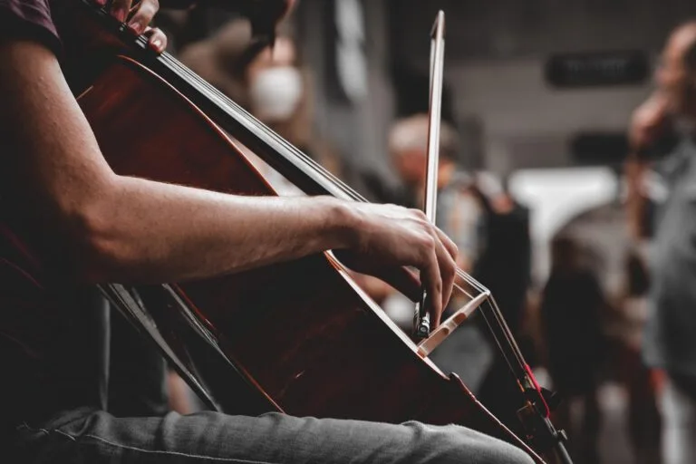 Lyrical Orchestra, gros plan sur les mains d’un violoncelliste jouant de son instrument dans un cadre urbain.
