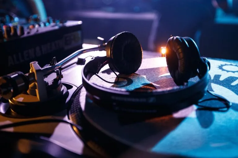 Casque audio posé sur une platine vinyle avec une table de mixage en arrière-plan, ambiance de club.