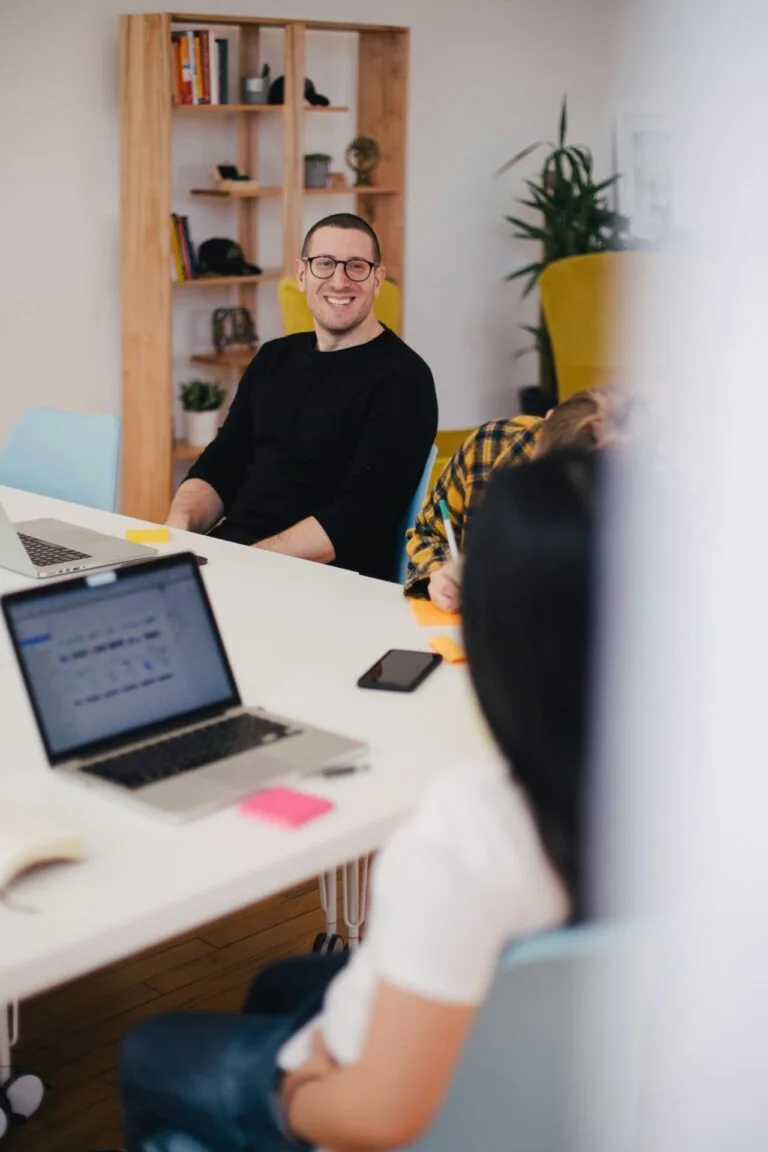 Réunion d'équipe dans un espace de coworking moderne avec un homme souriant en arrière-plan.
