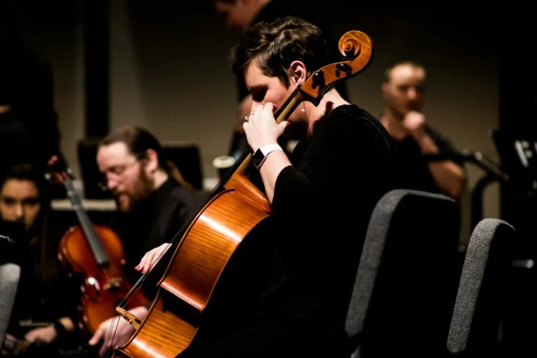 Lyrical Orchestra, violonniste concentrée jouant du violoncelle lors d’un concert classique, entourée d’autres musiciens.
