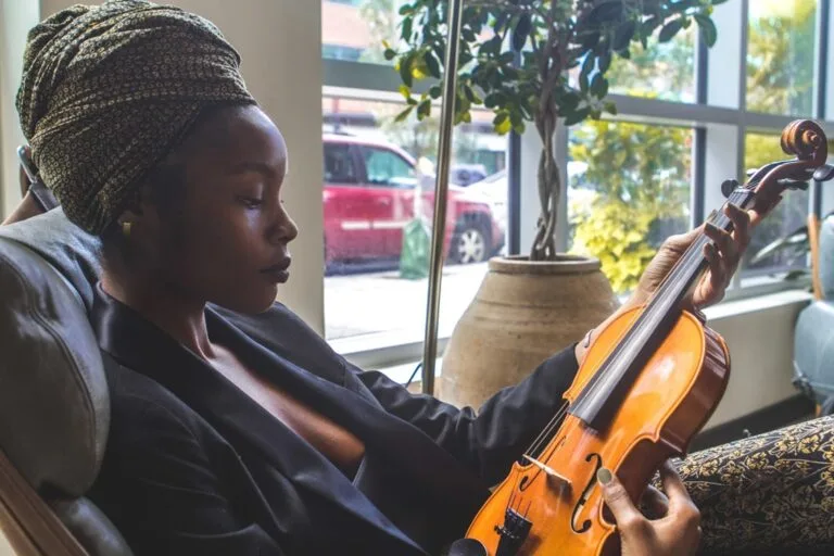 Lyrical Orchestra, femme élégante tenant un violon avec sérénité, assise dans un salon lumineux.