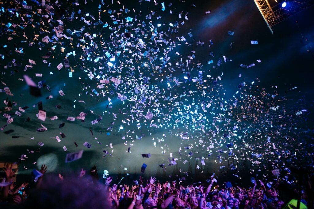 Foule en liesse sous une pluie de confettis colorés lors d’un concert nocturne.