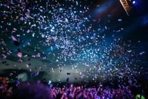Foule en liesse sous une pluie de confettis colorés lors d’un concert nocturne.